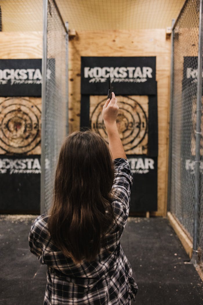Young woman throws an axe at a target in an indoor range, showcasing skill and focus.